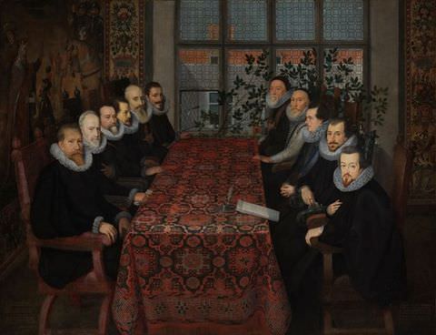 Painting. An interior scene featuring a long table covered by a red patterned tablecloth, seen at a slightly oblique angle, with seated men lined up on its left and right sides – six men on the left – and five men on the right. The men wear black gowns, and white, stiff ruffled collars and sit on tall backed wooden chairs. In the background lead lined windows reveal the street beyond.