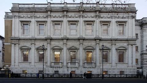 Colour photograph. A photograph of a large and wide rectangular building façade, with three storeys and multiple large sash windows. The building has a flat roof, and is decorated on the exterior with a series of pillars and orders.