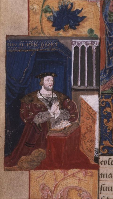 Photograph. In this illustration, we see a kneeling man wearing a thick red cape that has a fur trim, along with a small black hat. His hands are held together as if praying, and a small book is laid open on a low stool in front of him. Architectural features can just be seen behind him, including a row of pillars and a blue curtain.