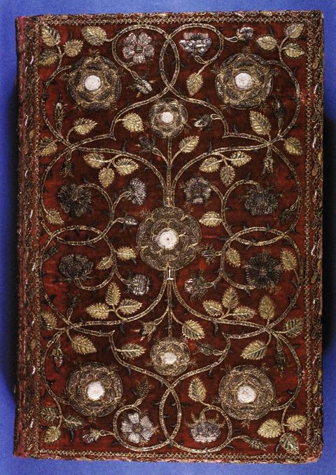 Embellished book cover. Late sixteenth-century Bible bound in deep red velvet, richly embroidered with gold and silver thread in a symmetrical design of scrolling vines, leaves, and large stylised flowers with pale centres; a narrow ornamental border frames the cover, and the textile surface shows slight wear, reflecting its ceremonial presentation to Queen Elizabeth I.