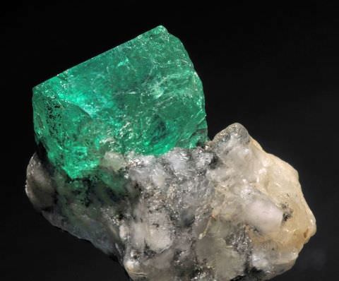 Colour photograph. An object resembling a rock or crystal, with a lower white and grey section and an upper green area is photographed from a close-up view against a stark black background. 